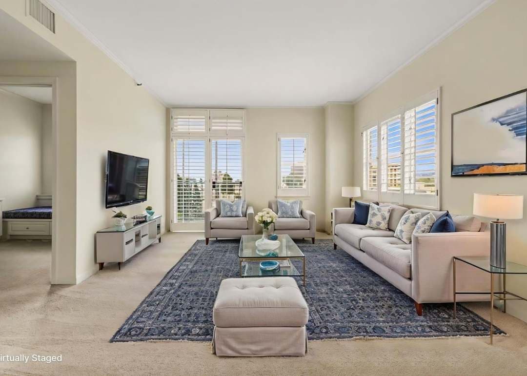 Condo living room tastefully staged with large windows, large couch, and tv.