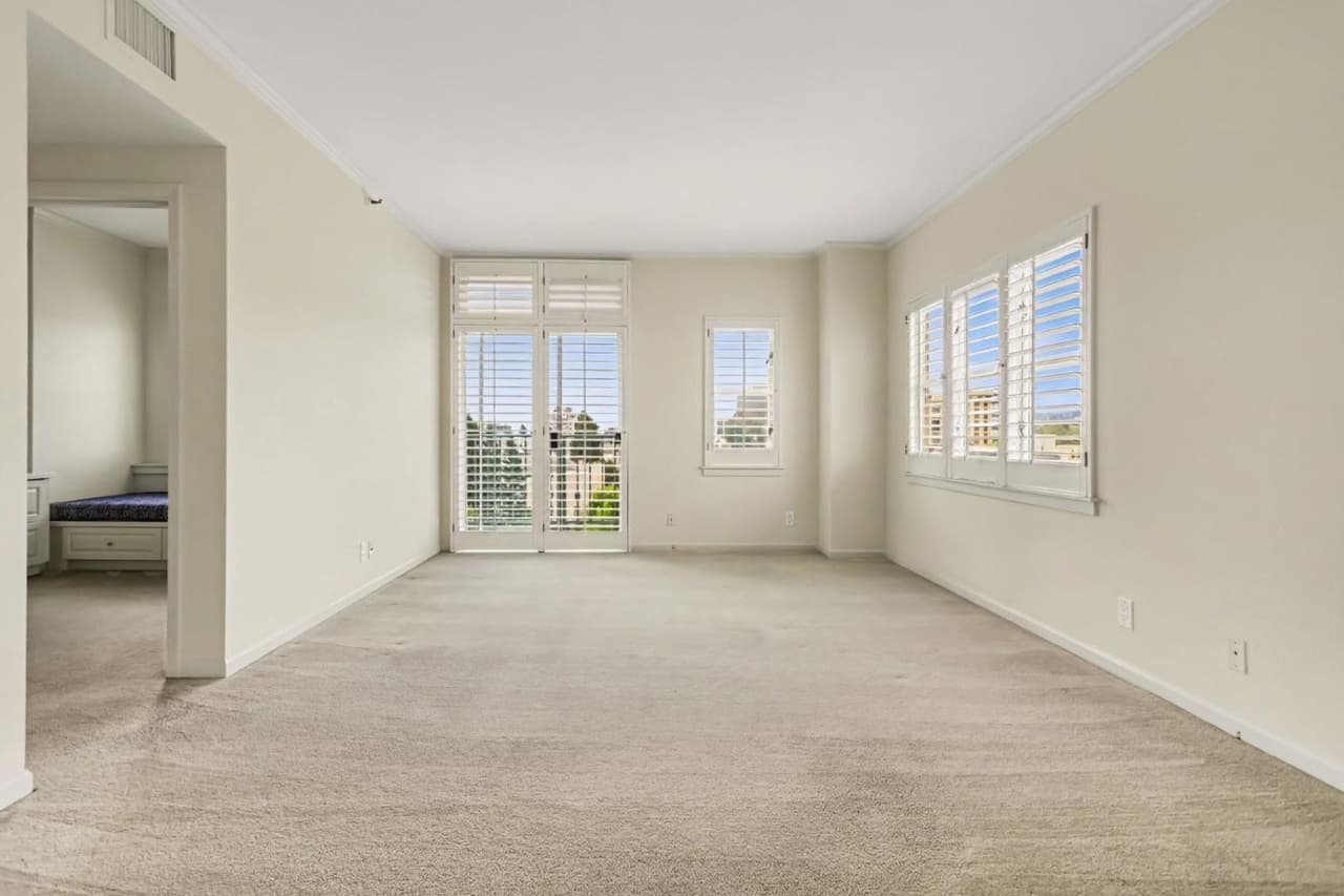 Condo living room with carpet, many windows and without furniture